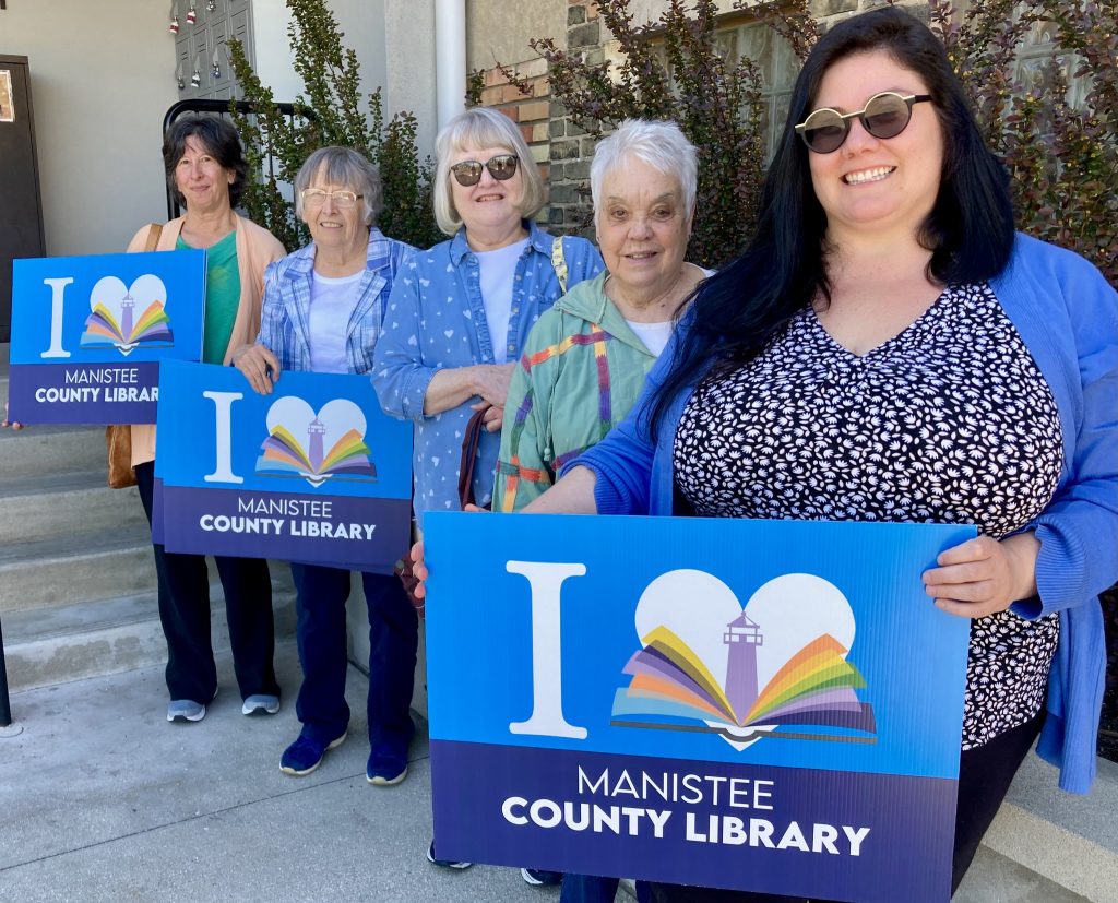 Women holding yard signs that say "I heart manistee county library"