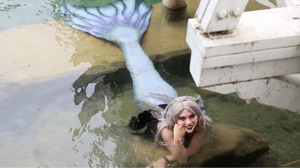 Woman cosplaying as a mermaid laying on rocks in water
