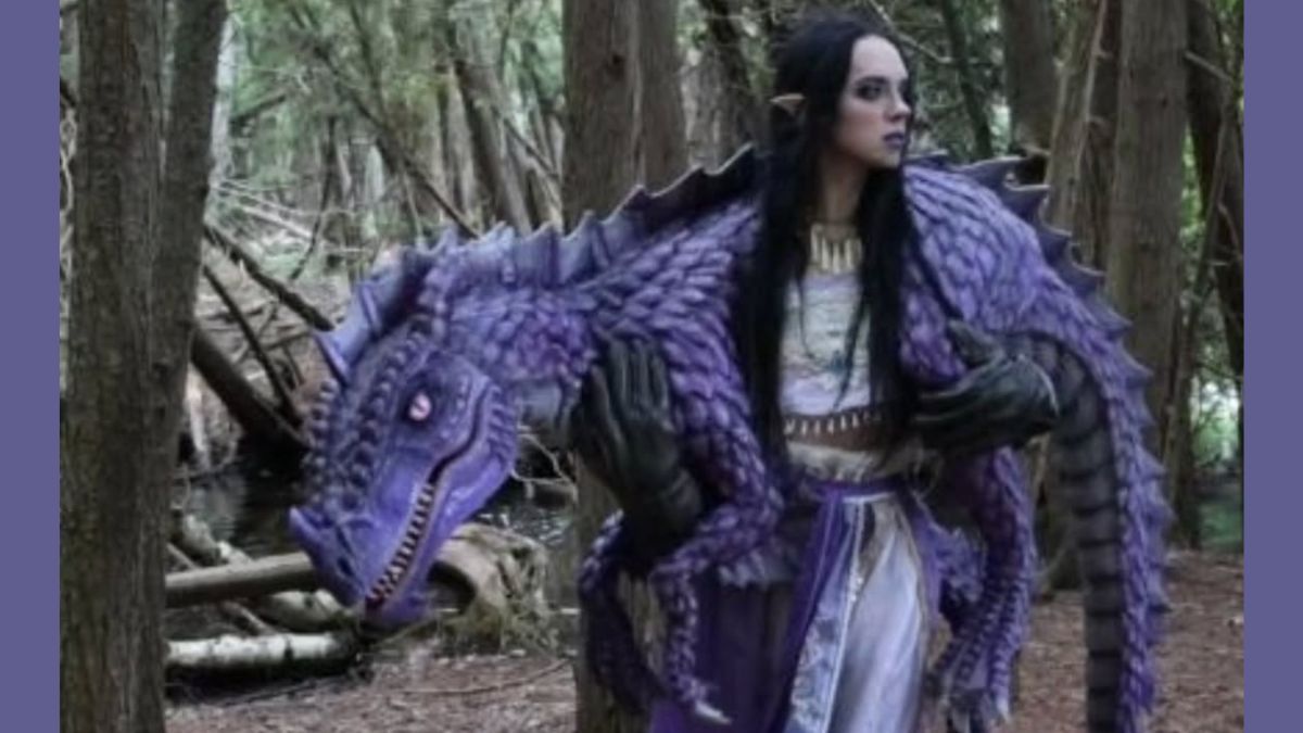 Elvish woman holds purple animatronic dragon over her shoulder in the forest