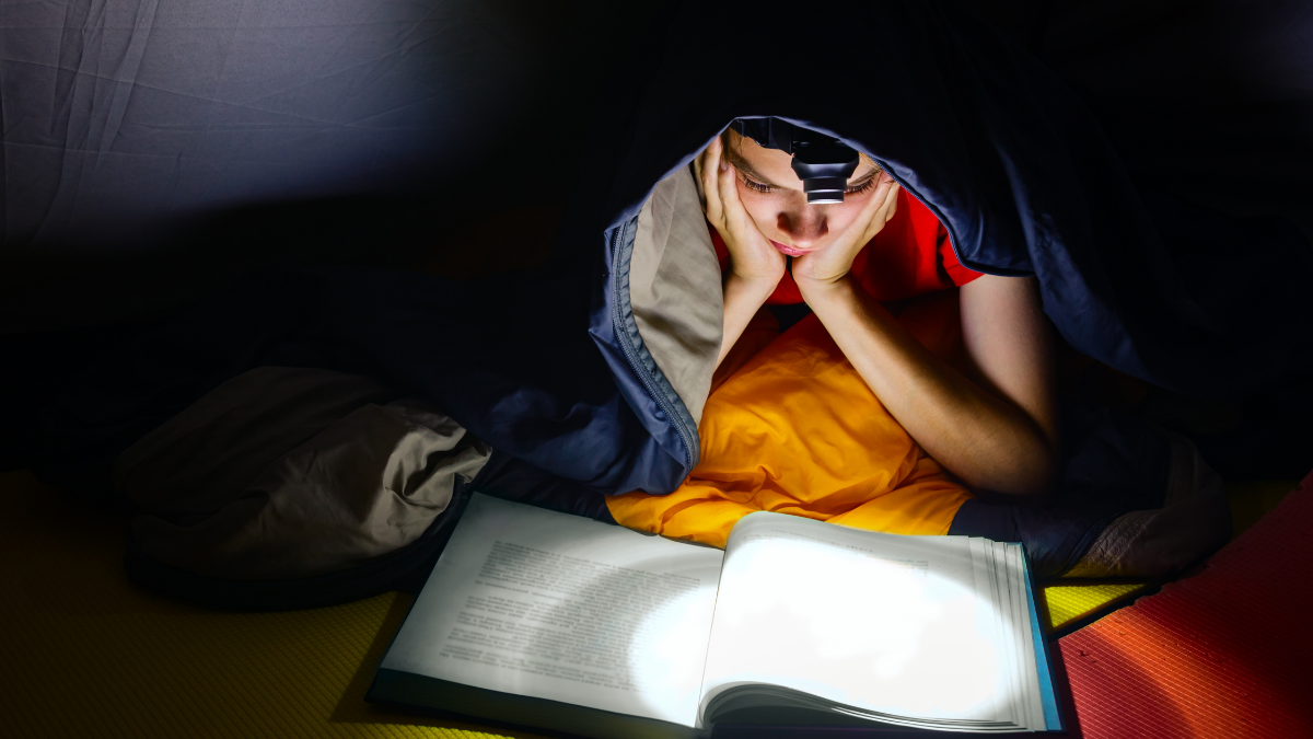 kid reading book with headlamp